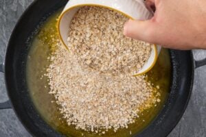 Oats being poured on top of the melted butter mixture in a cast iron pan